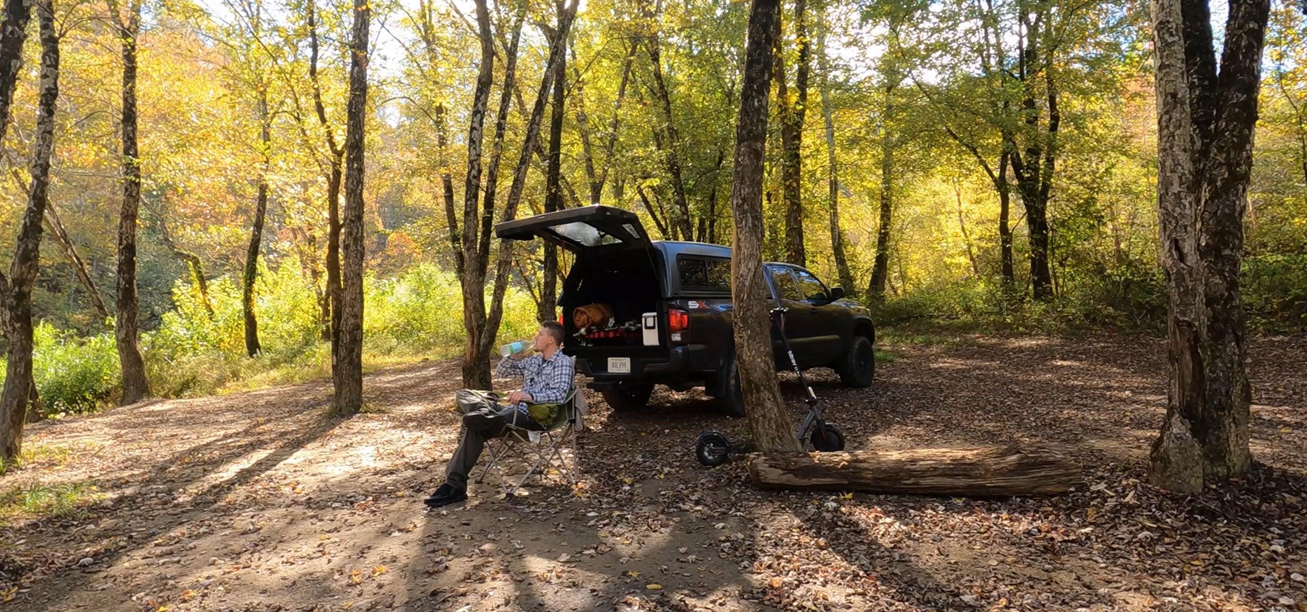 Man relaxing by truck in autumn forest campsite, enjoying outdoor wilderness.