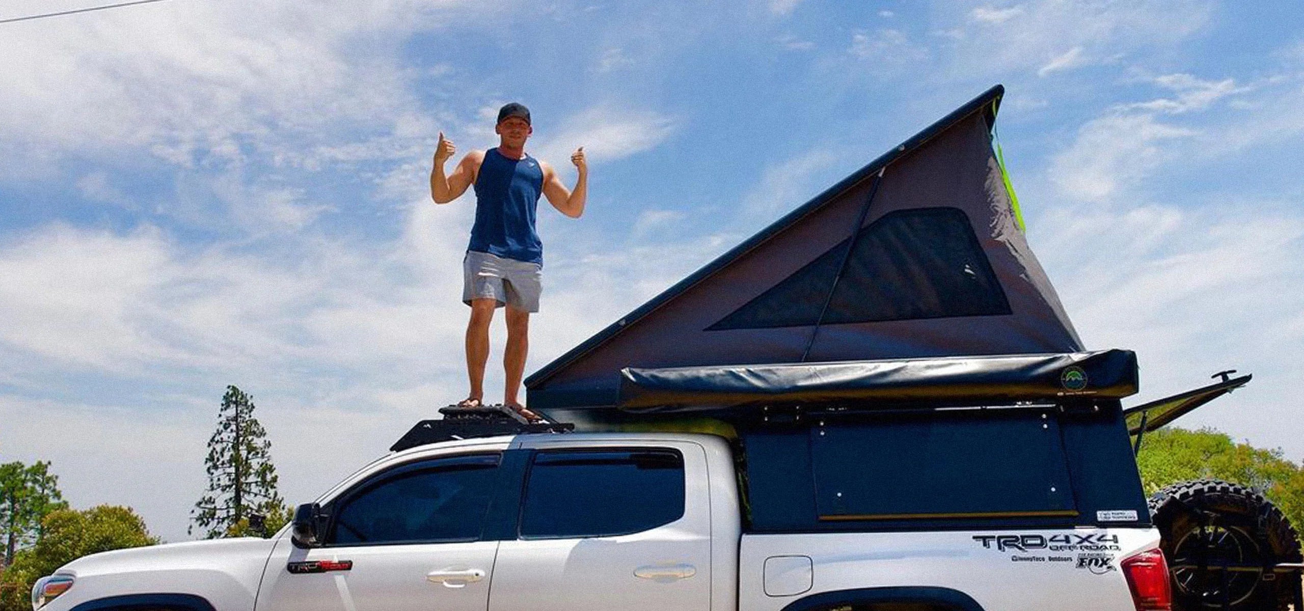 Man standing on a truck with rooftop tent, outdoor camping scene, blue sky background