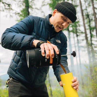 Man pouring coffee from Stoke Voltaics all-purpose kettle french press outdoors in forest