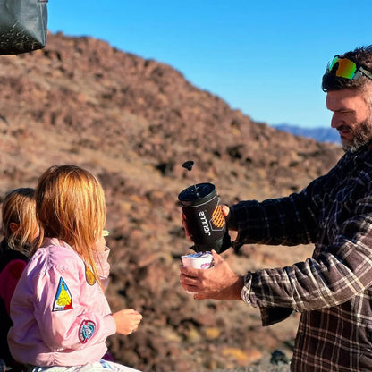 Man pours outdoor French press coffee into cup with kids in rocky wilderness, Stoke Voltaics