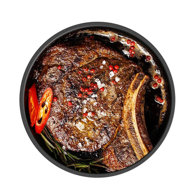Seared bone-in steak with red pepper, herbs, and seasoning in black outdoor cooking pan